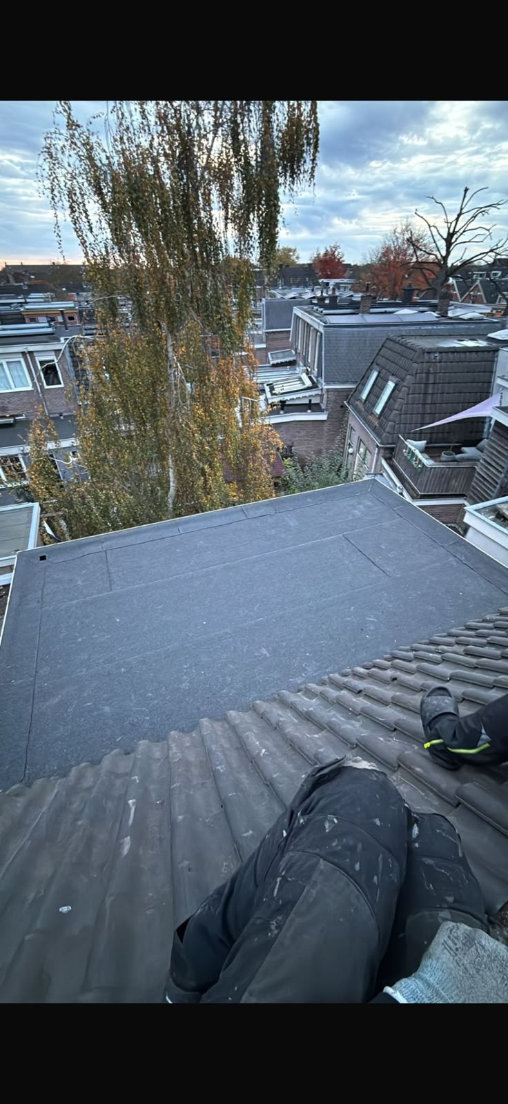 Afgewerkt bitumen plat dak naast een pannendak in een woonwijk